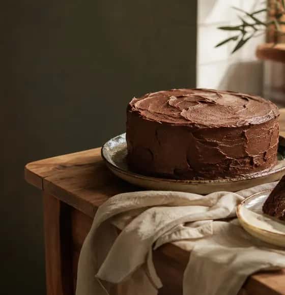Bolo de chocolate caseiro sobre uma mesa de madeira iluminada pelo sol