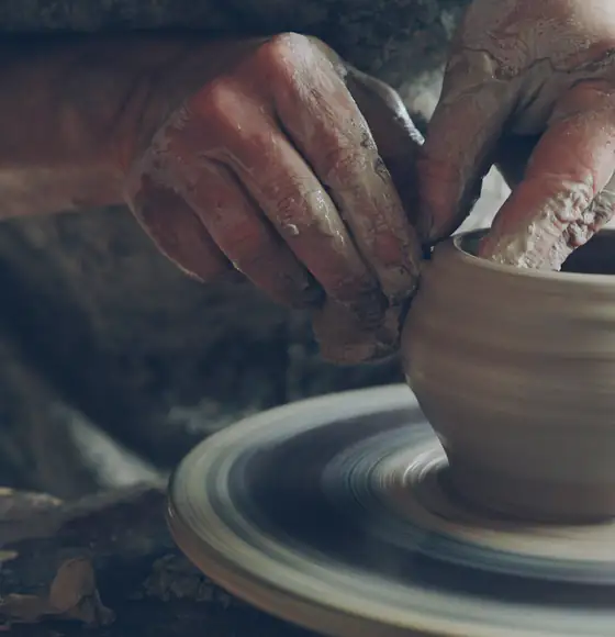 Mãos moldando uma peça de cerâmica em um torno de ateliê