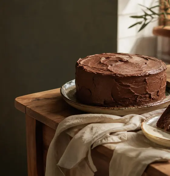 Bolo de chocolate caseiro sobre uma mesa de madeira iluminada pelo sol